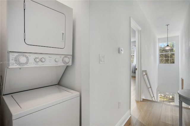 laundry room with baseboards, stacked washer and dryer, wood finished floors, and laundry area