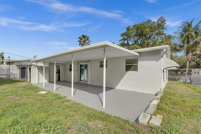 rear view of property featuring a lawn, fence, and stucco siding