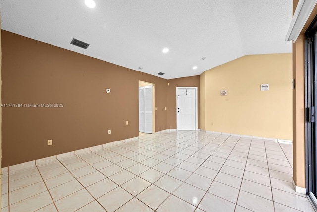 tiled empty room featuring vaulted ceiling and a textured ceiling