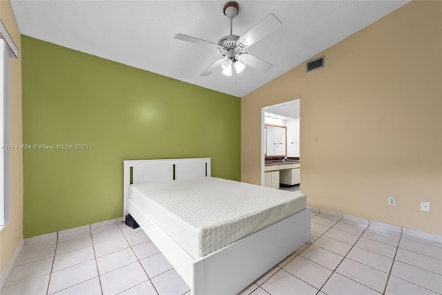 bedroom featuring light tile patterned flooring, lofted ceiling, ensuite bath, a textured ceiling, and ceiling fan