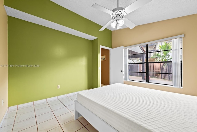 bedroom with vaulted ceiling, light tile patterned floors, ceiling fan, and a textured ceiling