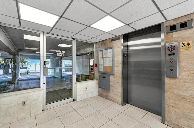 interior space with elevator, tile patterned floors, and a paneled ceiling