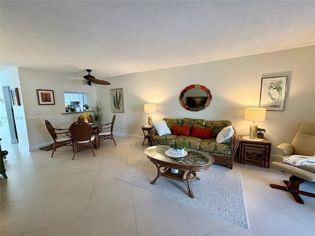 living room featuring ceiling fan, baseboards, a textured ceiling, and light tile patterned flooring