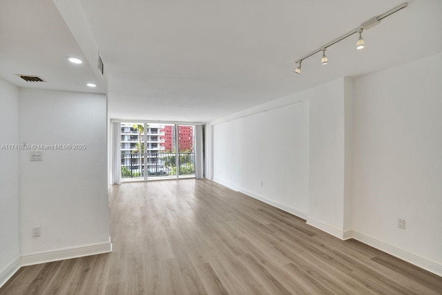 unfurnished room with floor to ceiling windows, track lighting, and light hardwood / wood-style floors