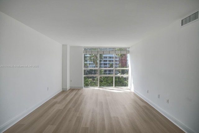 spare room with a wall of windows and light wood-type flooring