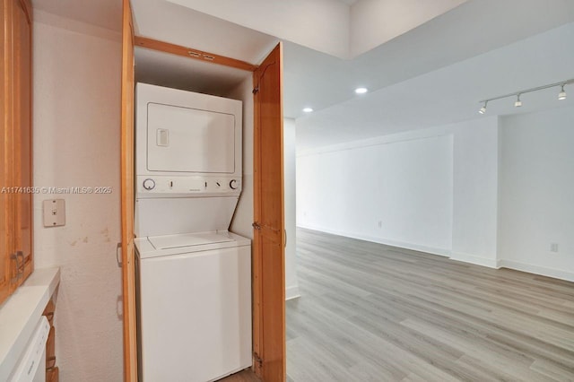 laundry area with stacked washer / drying machine, track lighting, and light hardwood / wood-style floors