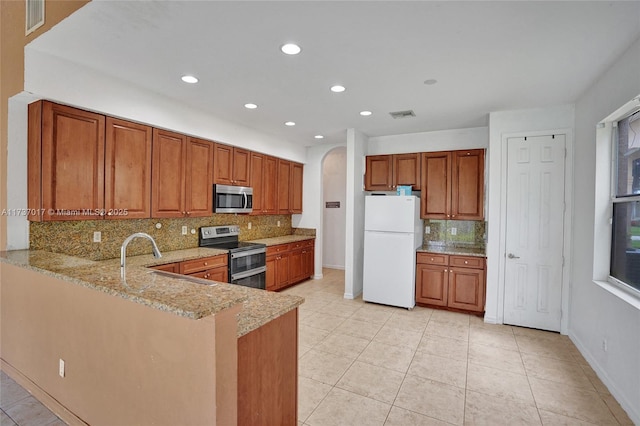 kitchen with sink, light stone counters, tasteful backsplash, appliances with stainless steel finishes, and kitchen peninsula