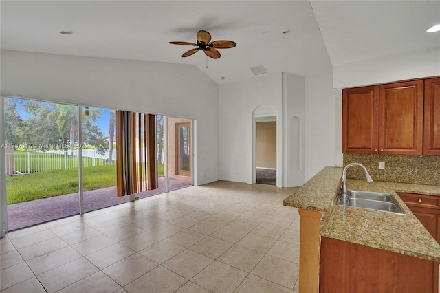 kitchen with sink, light tile patterned floors, light stone counters, decorative backsplash, and kitchen peninsula