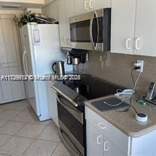 kitchen with light tile patterned floors, white cabinetry, range with electric stovetop, decorative backsplash, and white fridge