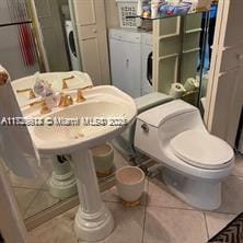 bathroom with independent washer and dryer, tile patterned floors, and toilet