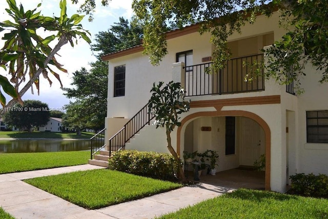 exterior space featuring a water view, a balcony, and a lawn