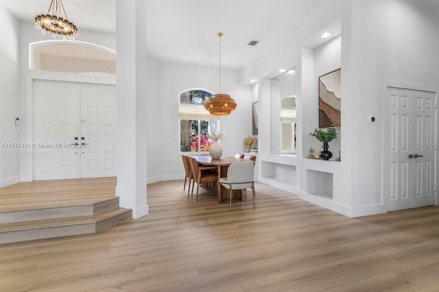 dining area featuring built in shelves, a chandelier, a high ceiling, and light wood-type flooring