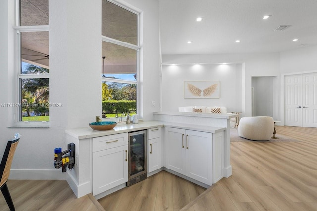 bar featuring light hardwood / wood-style flooring, beverage cooler, and white cabinets