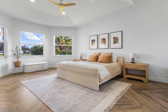 bedroom with a raised ceiling, parquet flooring, and ceiling fan