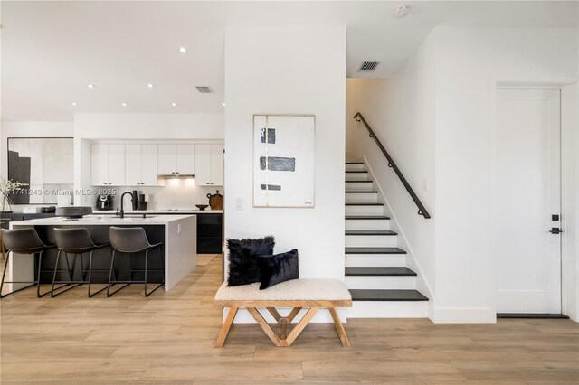 kitchen featuring light wood-type flooring, a kitchen breakfast bar, a kitchen island with sink, and white cabinets