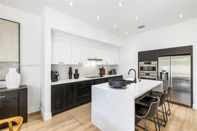 kitchen featuring stainless steel appliances, light hardwood / wood-style floors, a kitchen island with sink, and a breakfast bar area