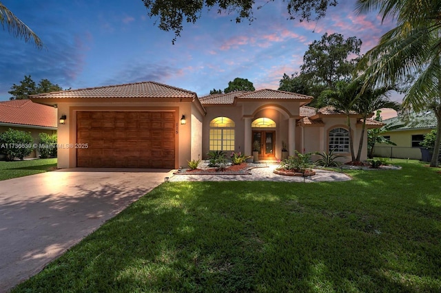 mediterranean / spanish-style house featuring a front lawn, a tile roof, concrete driveway, stucco siding, and an attached garage