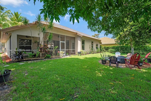 rear view of house featuring stucco siding, ceiling fan, a fire pit, and a yard