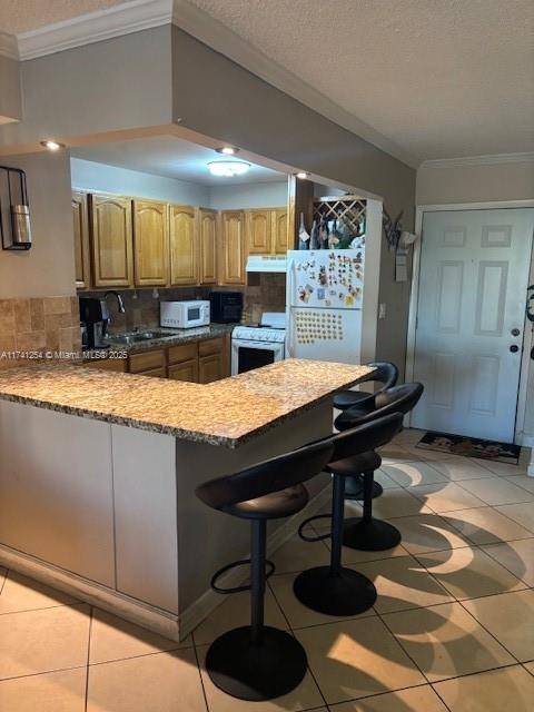 kitchen featuring sink, white appliances, a kitchen breakfast bar, ornamental molding, and kitchen peninsula