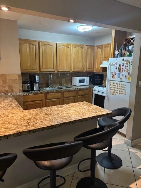 kitchen featuring a kitchen bar, sink, light tile patterned floors, white appliances, and decorative backsplash