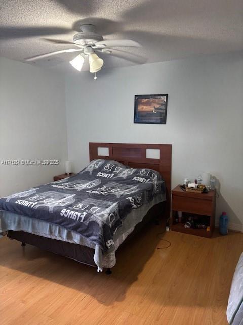 bedroom with ceiling fan, hardwood / wood-style flooring, and a textured ceiling