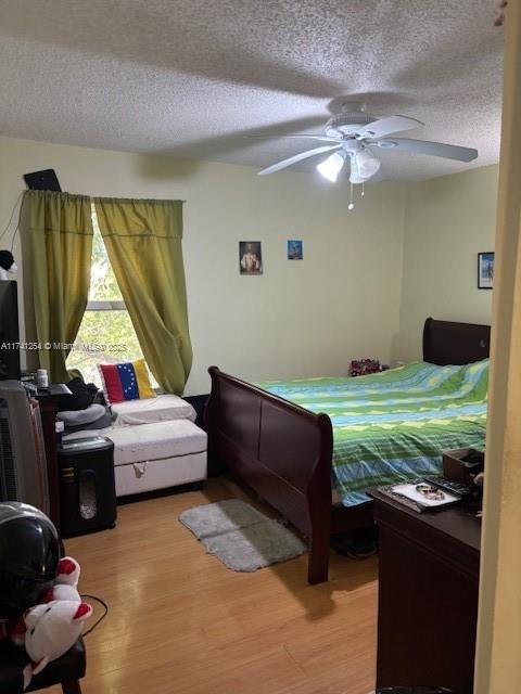 bedroom featuring ceiling fan, hardwood / wood-style floors, and a textured ceiling