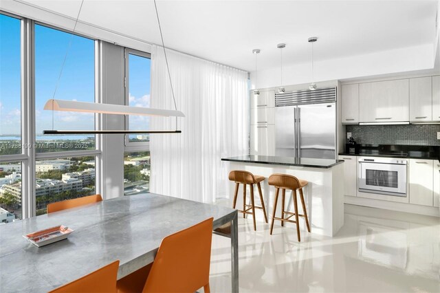 kitchen featuring a kitchen bar, built in refrigerator, hanging light fixtures, expansive windows, and wall oven