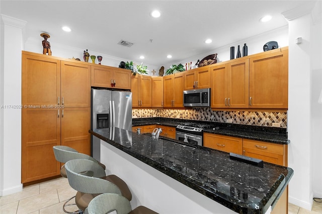 kitchen featuring tasteful backsplash, dark stone countertops, a kitchen breakfast bar, light tile patterned floors, and stainless steel appliances