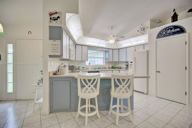 kitchen featuring light tile patterned flooring, a kitchen breakfast bar, kitchen peninsula, a raised ceiling, and white appliances