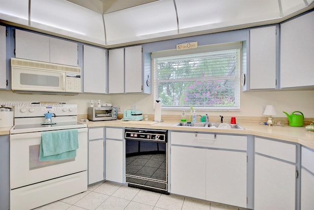 kitchen with sink, white appliances, light tile patterned floors, and white cabinets