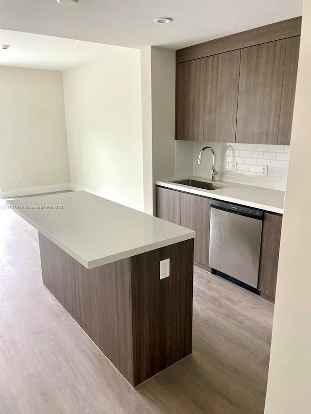 kitchen with sink, stainless steel dishwasher, a kitchen island, light hardwood / wood-style floors, and backsplash