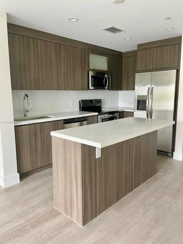 kitchen featuring sink, backsplash, stainless steel appliances, a center island, and light wood-type flooring