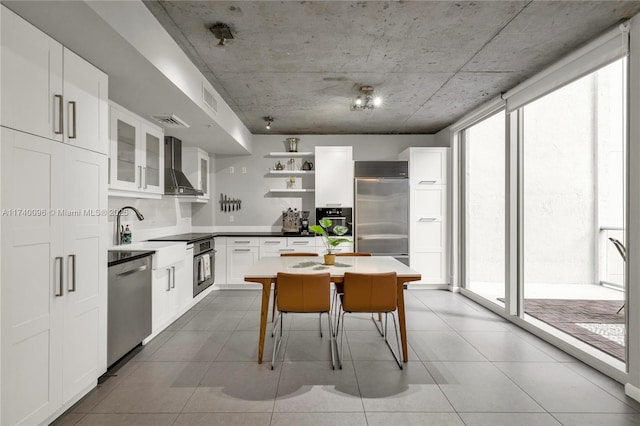 kitchen with tile patterned floors, stainless steel appliances, wall chimney exhaust hood, and white cabinets