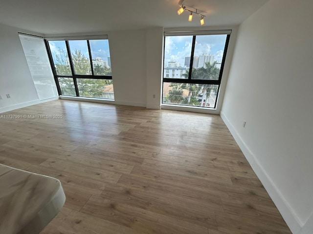 spare room with a wall of windows, track lighting, and light hardwood / wood-style flooring