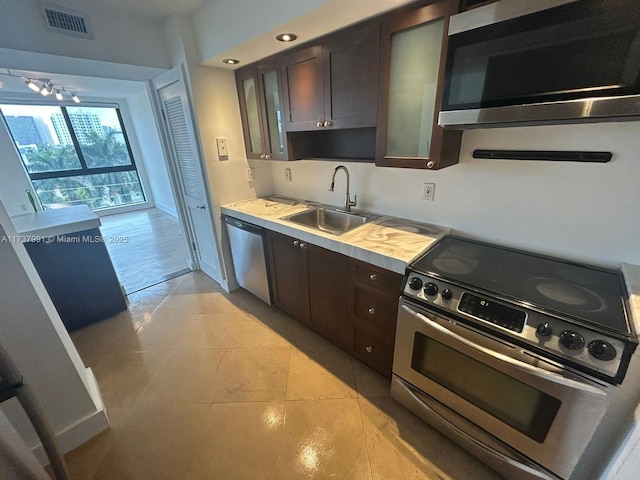 kitchen with sink, light tile patterned floors, dark brown cabinets, and appliances with stainless steel finishes