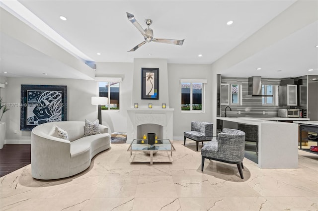 living room featuring a premium fireplace, plenty of natural light, sink, and ceiling fan