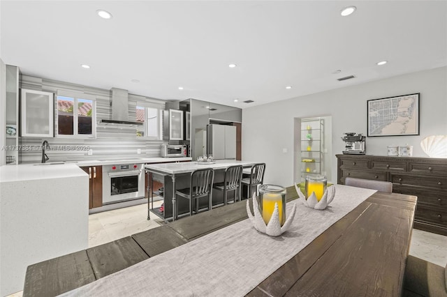 kitchen with wall chimney range hood, sink, a breakfast bar, a kitchen island, and stainless steel oven