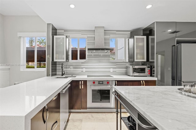 kitchen with appliances with stainless steel finishes, tasteful backsplash, sink, light stone counters, and wall chimney exhaust hood