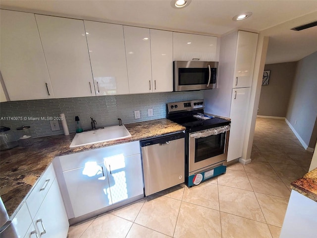 kitchen with light tile patterned floors, a sink, white cabinets, appliances with stainless steel finishes, and decorative backsplash