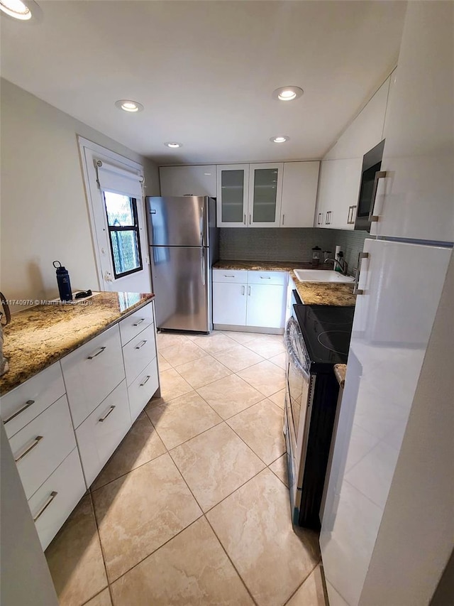kitchen featuring glass insert cabinets, a sink, white cabinetry, stainless steel appliances, and light stone counters