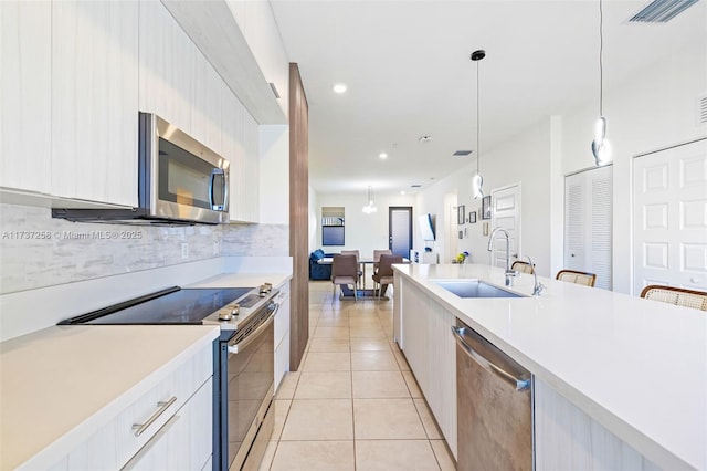 kitchen with pendant lighting, sink, white cabinets, light tile patterned floors, and stainless steel appliances