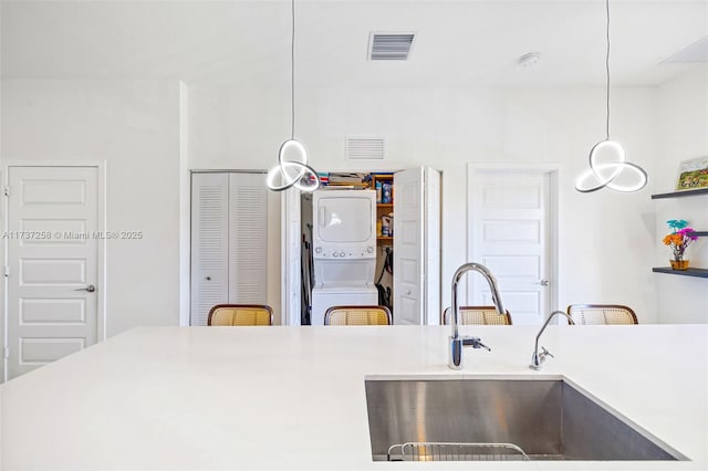 kitchen with stacked washer and clothes dryer, sink, and pendant lighting