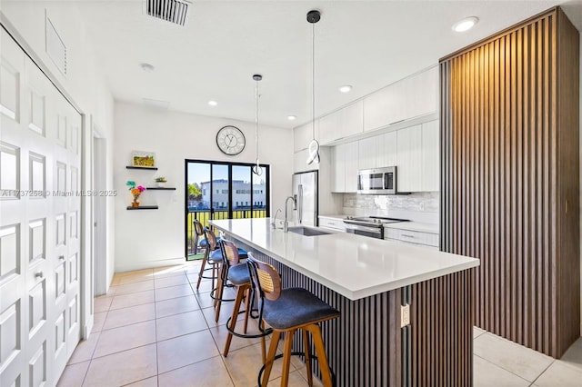 kitchen featuring sink, an island with sink, pendant lighting, stainless steel appliances, and white cabinets