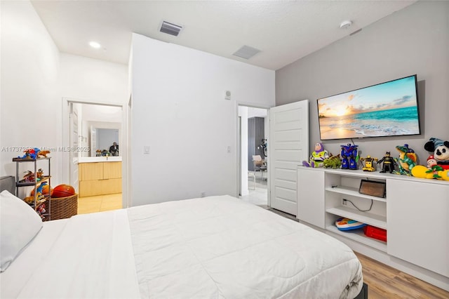 bedroom with ensuite bathroom, light hardwood / wood-style floors, and a textured ceiling