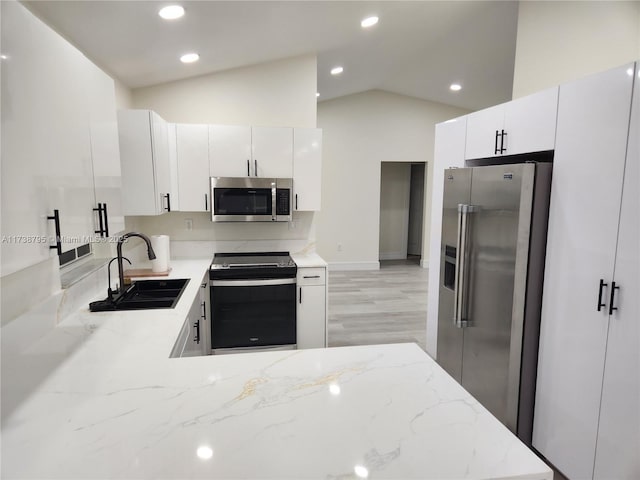 kitchen with lofted ceiling, sink, light stone counters, stainless steel appliances, and white cabinets