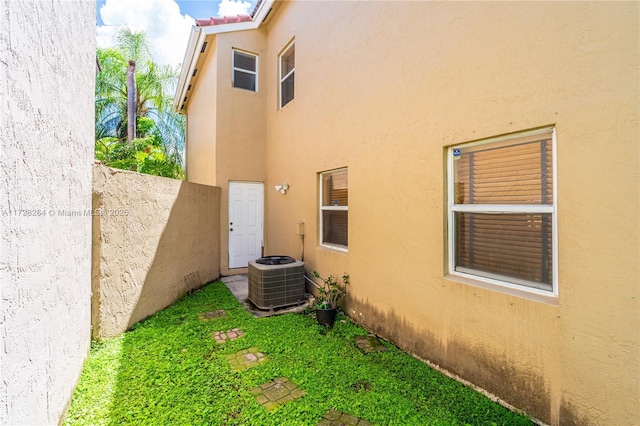 view of side of home featuring central AC, fence, and stucco siding