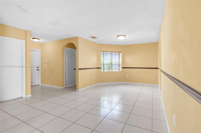 empty room with light tile patterned floors, visible vents, arched walkways, baseboards, and a textured ceiling