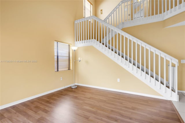 staircase featuring wood finished floors, a towering ceiling, and baseboards