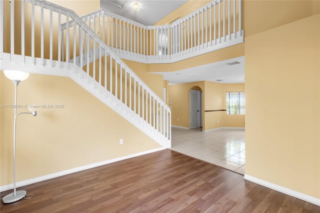 stairs featuring arched walkways, wood finished floors, a towering ceiling, visible vents, and baseboards