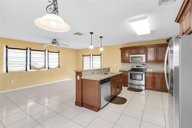 kitchen featuring brown cabinets, stainless steel appliances, a sink, and decorative light fixtures